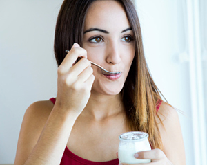 Image of a smiling woman eating yogurt after post oral surgery.