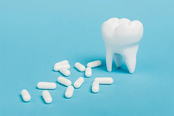 Artifical tooth next to white pills against a blue background at Masci, Hale & Wilson Advanced Aesthetic and Restorative Dentistry