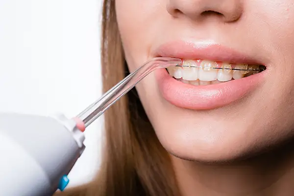 A woman using a water flosser to clean her teeth, demonstrating an effective oral hygiene tool.