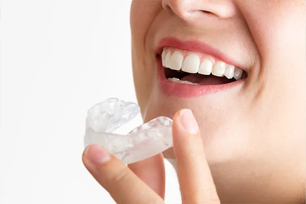 Close-up of a smiling woman holding a clear mouthguard near her teeth, showing how to prevent bruxism.