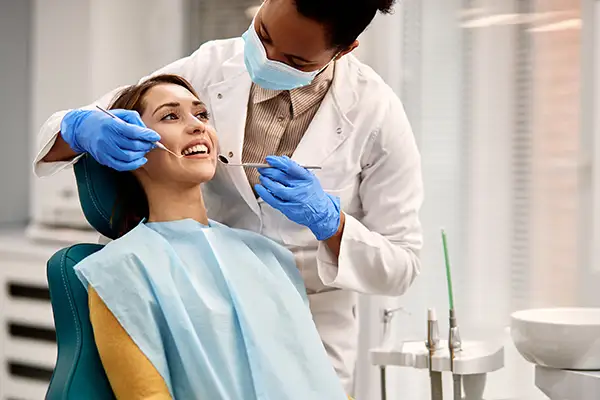 Dentist wearing gloves and a mask examining a smiling female patient during a dental checkup, emphasizing oral hygiene.