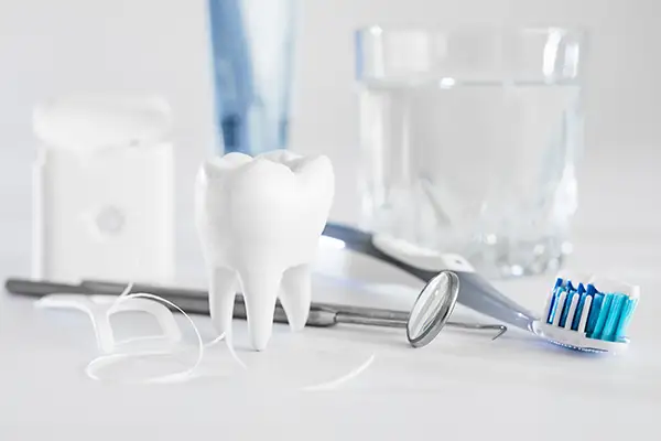 Dental tools, floss, and a model tooth displayed with a glass of water, promoting comprehensive oral hygiene practices.