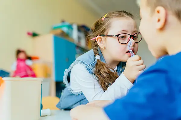 A young girl with special needs using a dental tool to check a boy's mouth during a playful activity practicing dental care.