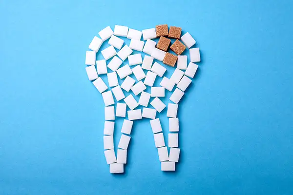 A tooth shape made of sugar cubes with brown sugar cubes at the top, illustrating tooth decay caused by a diet rich in sugar.